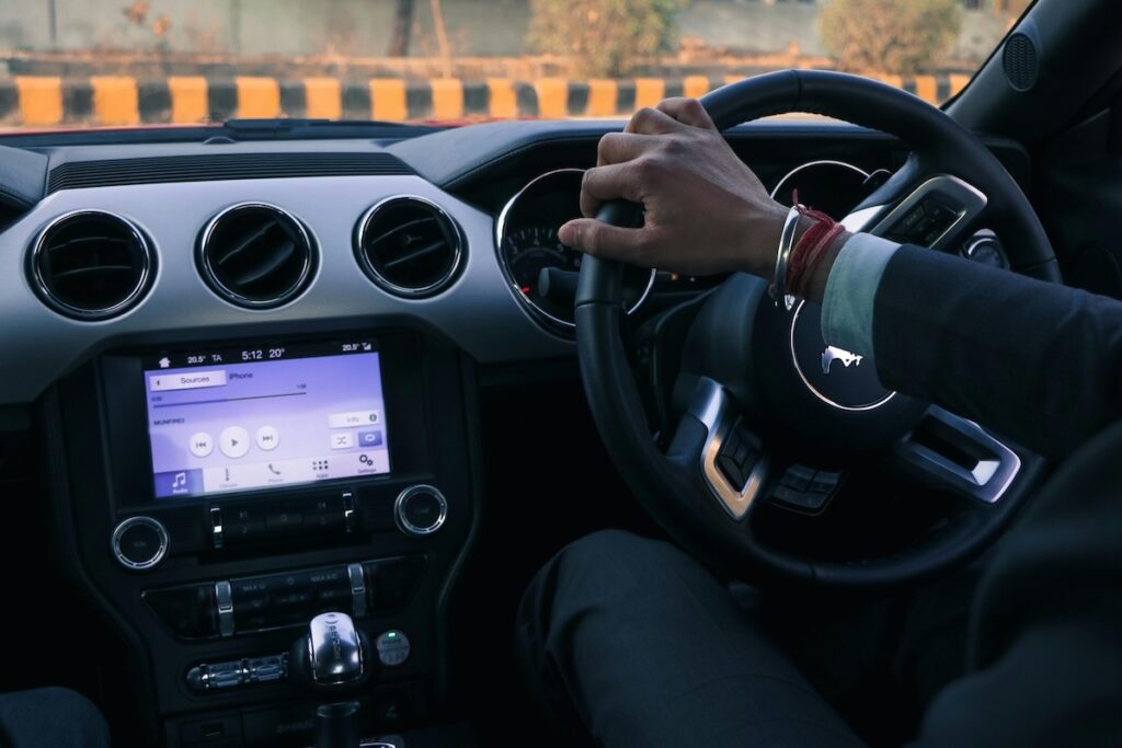 A person's hand on the steering wheel of a car, with the dashboard in the background.