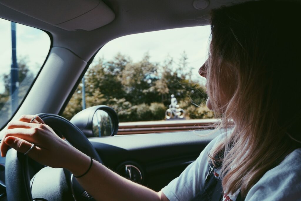  a woman driving a car on the right hand side, with her right hand on the steering wheel 